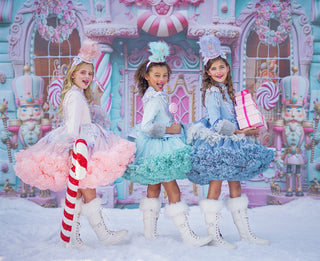 Three girls in pastel candy-themed tutus and boots posing before a Nutcracker sweet shop backdrop.